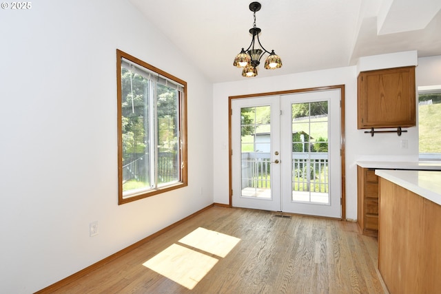 unfurnished dining area featuring french doors, plenty of natural light, light wood-style flooring, and vaulted ceiling