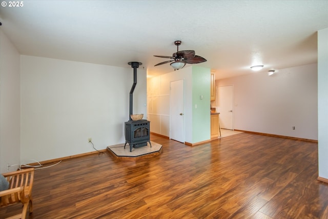 living area with a wood stove, ceiling fan, baseboards, and dark wood-type flooring