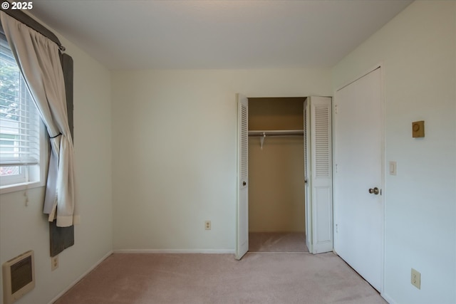 unfurnished bedroom with a closet, light carpet, baseboards, and heating unit