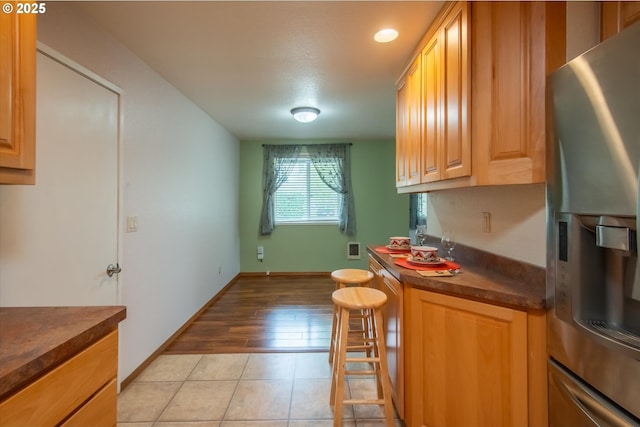 kitchen with dark countertops, light tile patterned floors, baseboards, and stainless steel refrigerator with ice dispenser