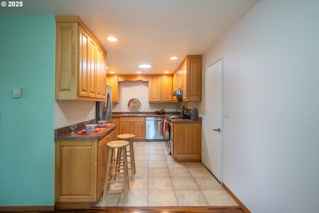 kitchen featuring a breakfast bar, dark countertops, recessed lighting, light brown cabinetry, and appliances with stainless steel finishes