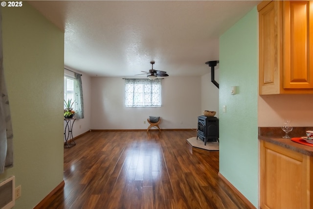 unfurnished living room featuring visible vents, dark wood-type flooring, a ceiling fan, a wood stove, and baseboards