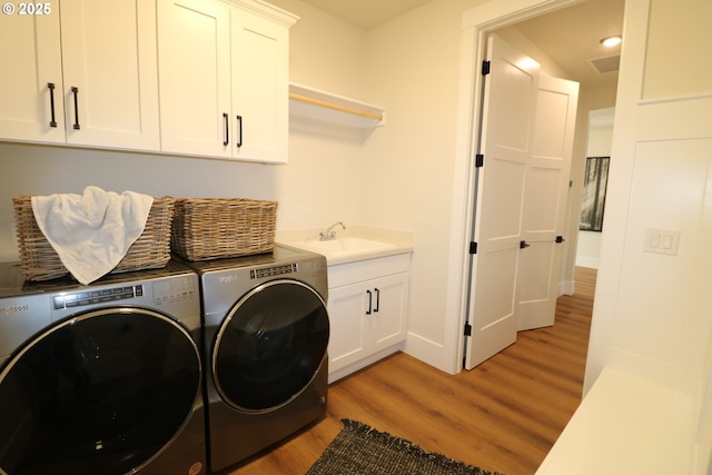 laundry area featuring cabinet space, light wood finished floors, baseboards, separate washer and dryer, and a sink