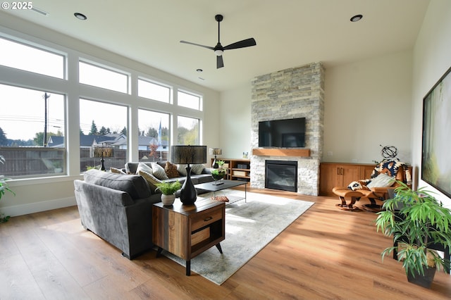 living room featuring ceiling fan, light wood-type flooring, and a stone fireplace