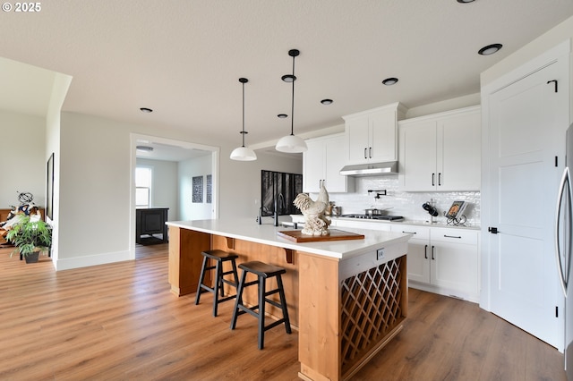 kitchen with hardwood / wood-style floors, stainless steel gas cooktop, a kitchen island with sink, white cabinets, and pendant lighting