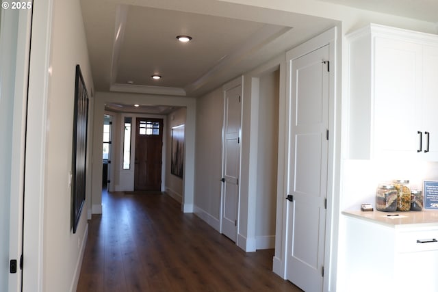 corridor with dark wood-style floors, baseboards, and a tray ceiling