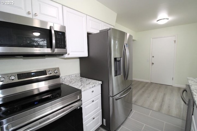 kitchen featuring light stone countertops, white cabinets, light hardwood / wood-style floors, and appliances with stainless steel finishes