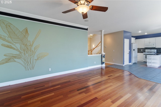 unfurnished living room with baseboards, ceiling fan, stairway, wood finished floors, and crown molding