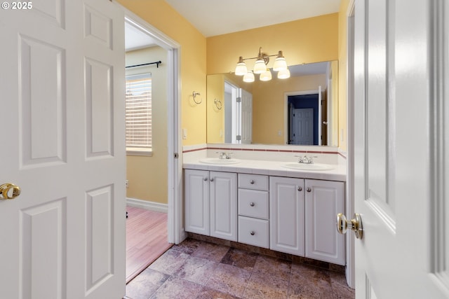 full bathroom featuring stone finish flooring, a sink, baseboards, and double vanity