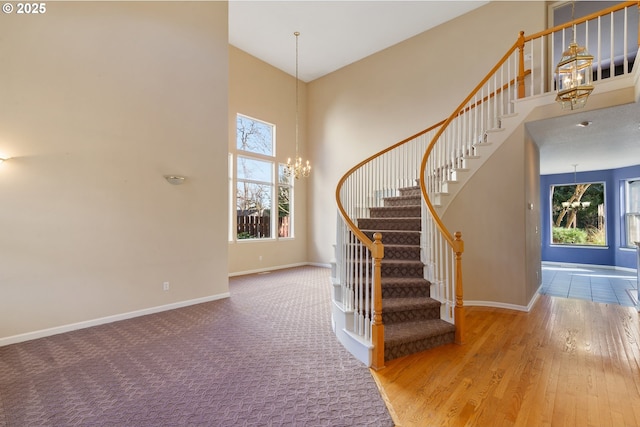 stairway featuring baseboards, a notable chandelier, a high ceiling, and wood finished floors