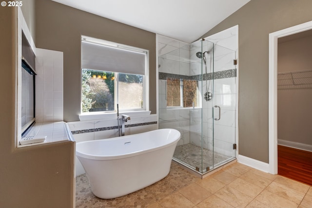 full bathroom featuring vaulted ceiling, a spacious closet, a stall shower, and a freestanding tub