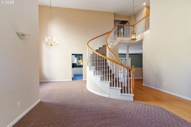 staircase with wood finished floors, carpet flooring, a towering ceiling, baseboards, and an inviting chandelier