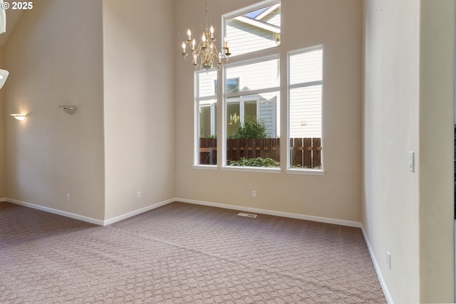 carpeted empty room with an inviting chandelier and baseboards