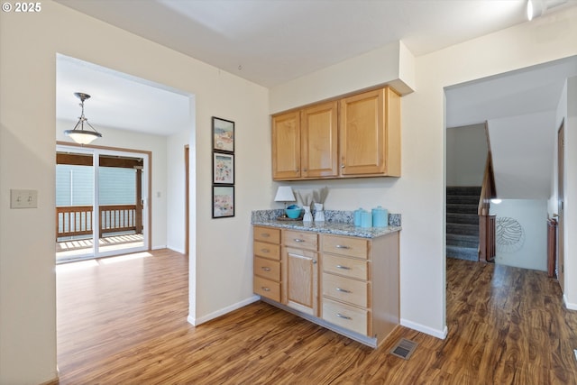 kitchen featuring light brown cabinetry, hanging light fixtures, light stone counters, and dark hardwood / wood-style floors