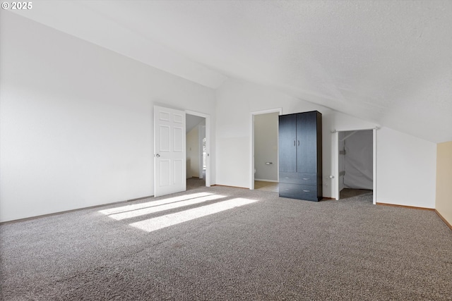 unfurnished bedroom with vaulted ceiling, a textured ceiling, and carpet flooring