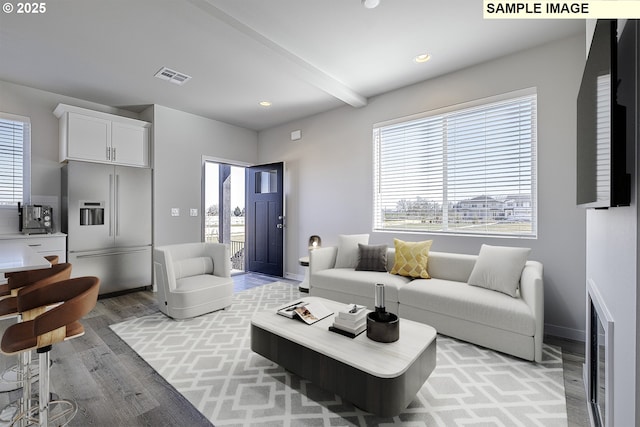 living area featuring a wealth of natural light, beam ceiling, visible vents, and light wood finished floors