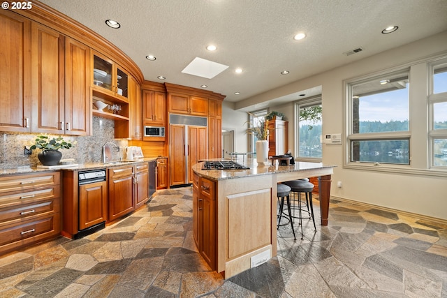 kitchen with a breakfast bar, a skylight, built in appliances, an island with sink, and decorative backsplash