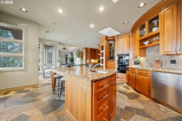 kitchen with sink, a breakfast bar area, black double oven, a center island with sink, and stainless steel dishwasher