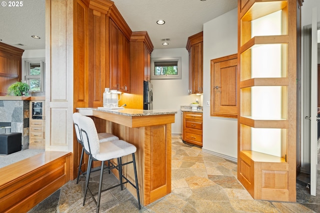 kitchen featuring fridge, a breakfast bar area, light stone counters, and kitchen peninsula