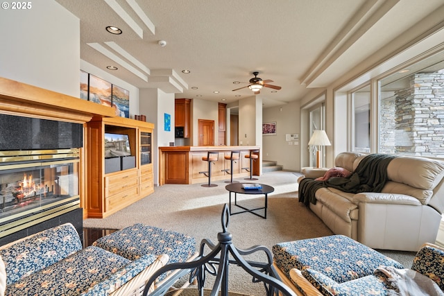 living room featuring ceiling fan, light colored carpet, and a textured ceiling