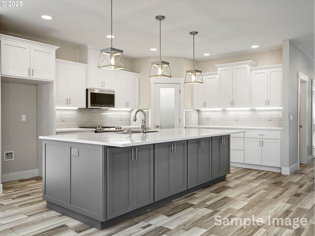 kitchen with a sink, light stone counters, white cabinetry, stainless steel appliances, and decorative backsplash