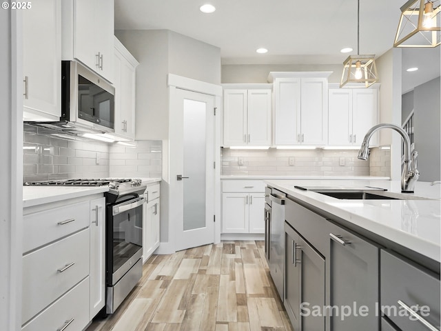 kitchen featuring light countertops, hanging light fixtures, white cabinets, stainless steel appliances, and a sink