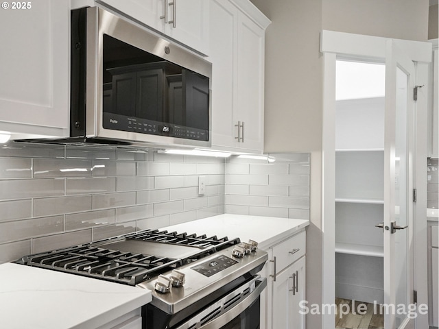 kitchen featuring white cabinets, backsplash, light stone countertops, and appliances with stainless steel finishes