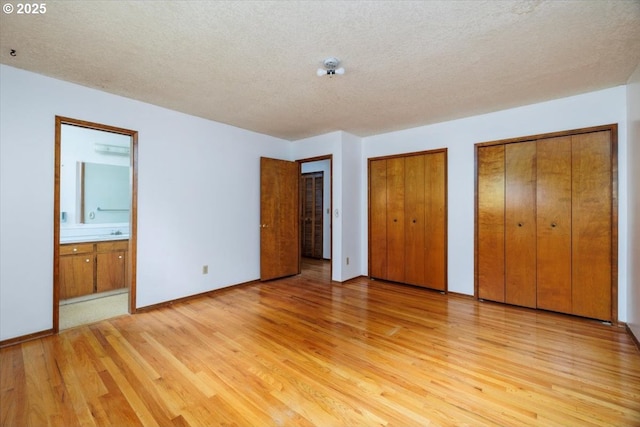 7450 SW Wilson Ave, Beaverton, OR 97008 - unfurnished bedroom with light wood-style flooring, multiple closets, a textured ceiling, connected bathroom, and baseboards