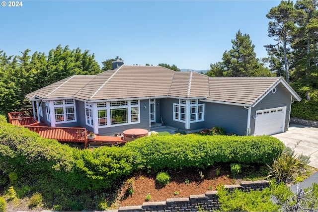ranch-style home with a tile roof, a wooden deck, concrete driveway, a garage, and a chimney