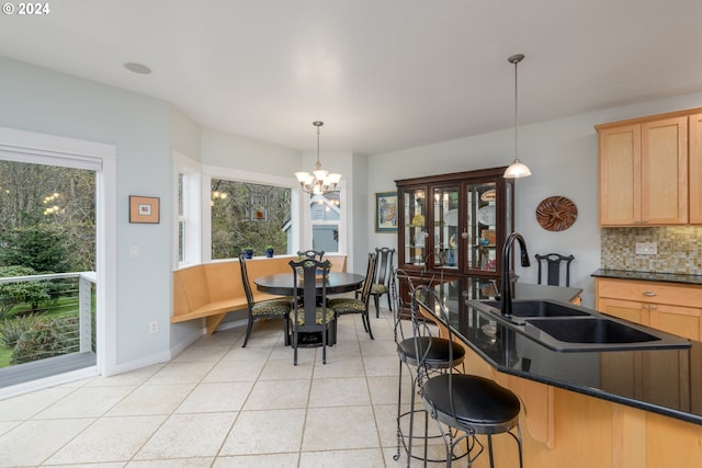 kitchen with light tile patterned floors, a sink, backsplash, dark countertops, and decorative light fixtures