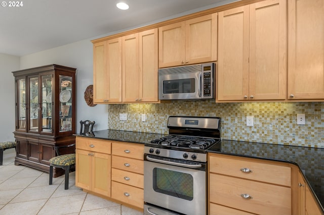 kitchen with light brown cabinetry, appliances with stainless steel finishes, and dark stone countertops