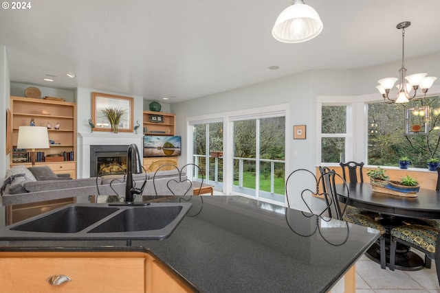 kitchen with a glass covered fireplace, dark countertops, open floor plan, hanging light fixtures, and a sink