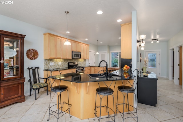 kitchen featuring dark countertops, appliances with stainless steel finishes, a sink, a peninsula, and a kitchen breakfast bar