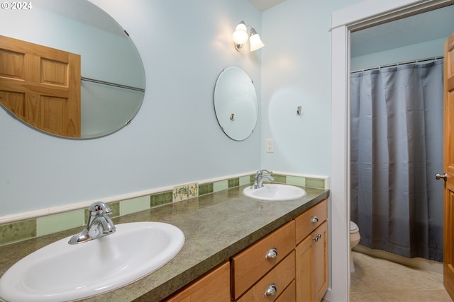 full bath featuring toilet, tile patterned flooring, double vanity, and a sink