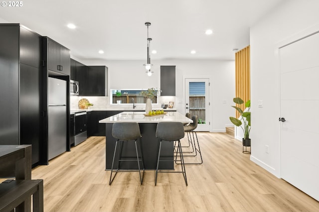 3528 NE 44th Ave, Portland, OR 97212 - kitchen featuring dark cabinetry, stainless steel appliances, light countertops, a kitchen breakfast bar, and light wood-style floors