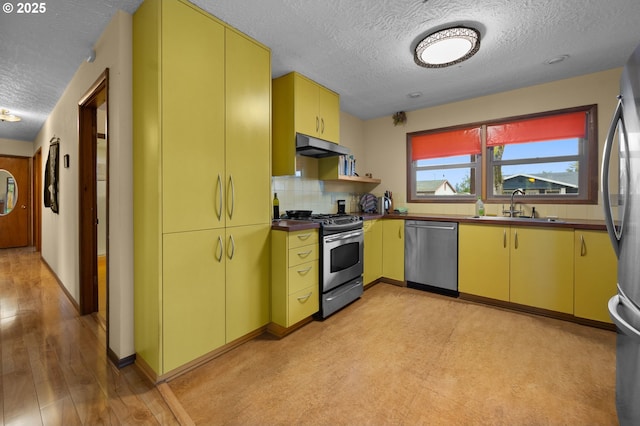 kitchen with a sink, under cabinet range hood, appliances with stainless steel finishes, and yellow cabinetry