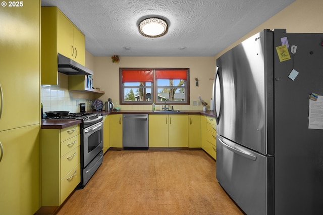 kitchen featuring yellow cabinets, a sink, stainless steel appliances, under cabinet range hood, and dark countertops