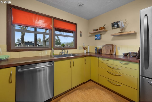 kitchen with a sink, open shelves, dark countertops, yellow cabinets, and appliances with stainless steel finishes