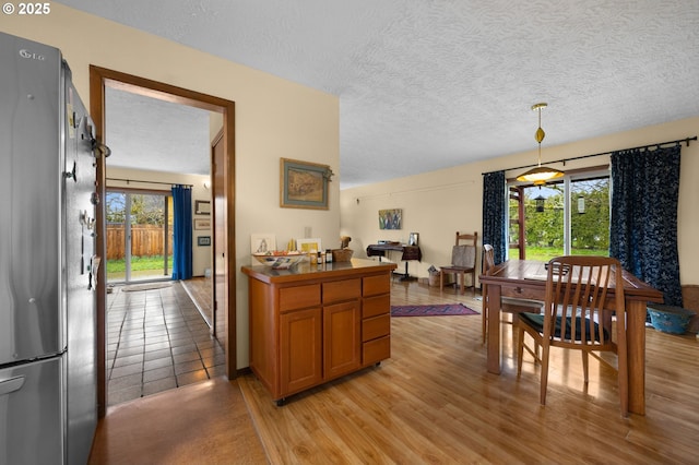 kitchen with a textured ceiling, brown cabinets, freestanding refrigerator, pendant lighting, and light wood-type flooring