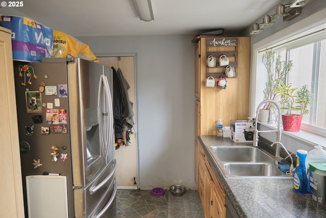 kitchen with dark countertops, stone finish flooring, stainless steel fridge, and a sink