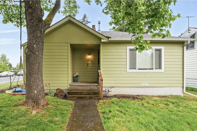 view of front of property with fence, roof with shingles, and a front lawn