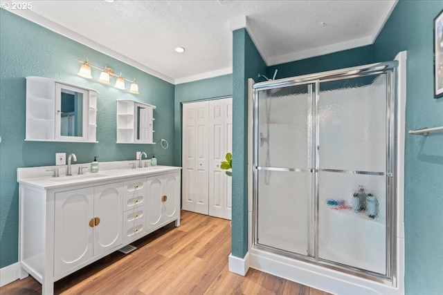 bathroom featuring wood finished floors, a textured wall, a sink, and a stall shower