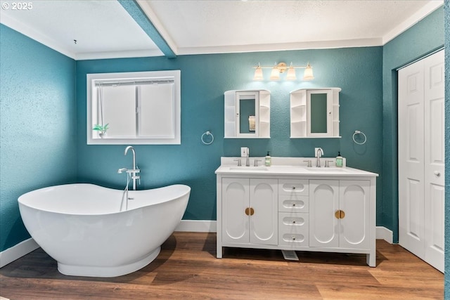 bathroom featuring double vanity, wood finished floors, baseboards, a freestanding bath, and a sink