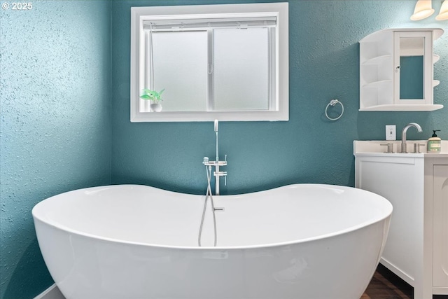 bathroom with a freestanding tub, a textured wall, vanity, and wood finished floors