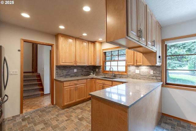 kitchen featuring stone finish floor, light brown cabinets, backsplash, and a sink