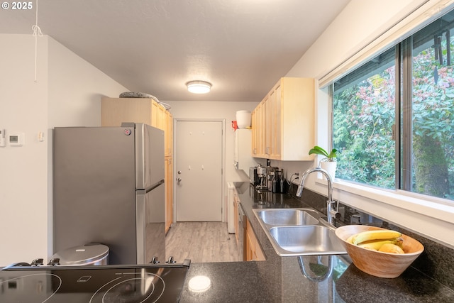 kitchen with dark countertops, light wood finished floors, light brown cabinetry, appliances with stainless steel finishes, and a sink