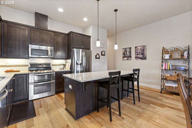 16033 SW 2nd St, Sherwood, OR 97140 - kitchen with stainless steel appliances, light wood-style flooring, dark brown cabinets, a breakfast bar, and light stone countertops
