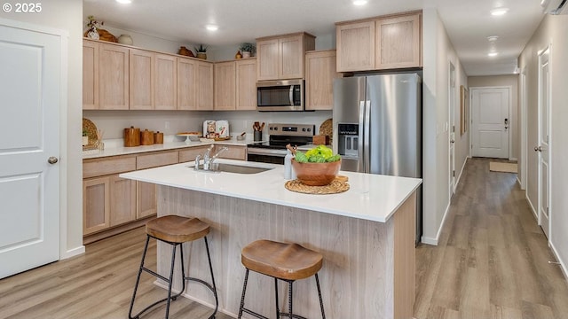 kitchen with appliances with stainless steel finishes, a kitchen bar, sink, and light brown cabinets