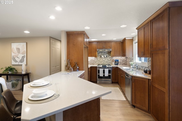 kitchen featuring appliances with stainless steel finishes, a peninsula, light countertops, light wood finished floors, and recessed lighting