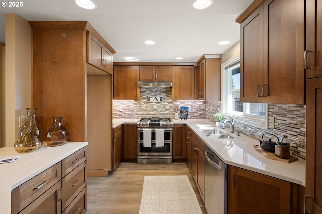 kitchen with appliances with stainless steel finishes, brown cabinets, light wood-style flooring, a sink, and recessed lighting
